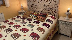 Een bed met een geborduurde quilt, een versierd hoofdbord, twee nachtkastjes met lampen en een ingelijste foto aan de muur.