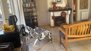 Een gezellige woonkamer met een open haard, een boekenkast, een schommelstoel en een houten bankje.