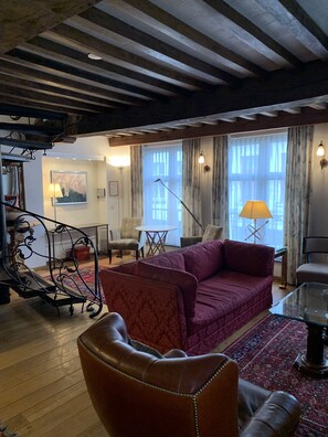 A cozy living room with a red sofa, a glass coffee table, and a wooden floor. There is a staircase with a wrought iron railing leading to another level. - Cosy quality two storey holiday flat in medieval city centre, Casa Michelangelo (BRUGES)