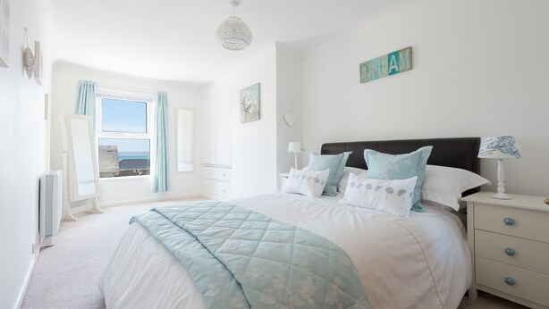 Un dormitorio con una cama grande, una mesita de noche, una lámpara, una ventana con cortinas y una pared con un letrero que dice 'DREAM'.