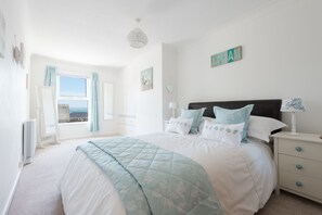 Une chambre avec un grand lit, une table de chevet, une lampe, une fenêtre avec des rideaux et un mur orné d’un panneau indiquant le mot « RÊVE ».
