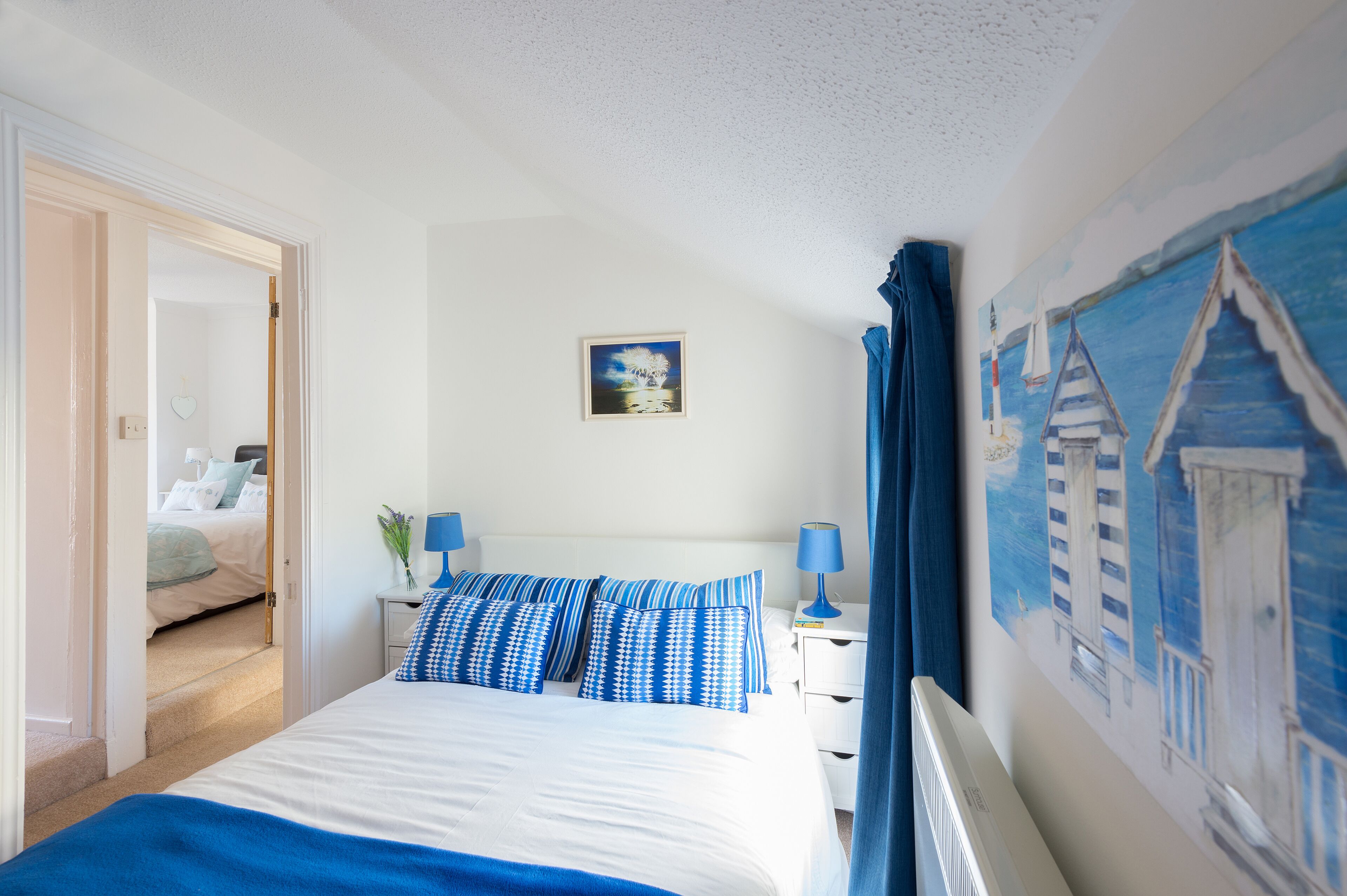 Una camera da letto con un letto, un comodino, una lampada, un quadro e una porta che dà su un'altra stanza.
