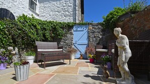 Un patio de piedra con un banco, una estatua y plantas en macetas.