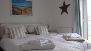 A neatly made bed with white bedding and striped pillows, a star decoration on the wall, and a painting of a beach scene above the bed. - Filey. Active leisure or relaxing beach holiday. (Filey)