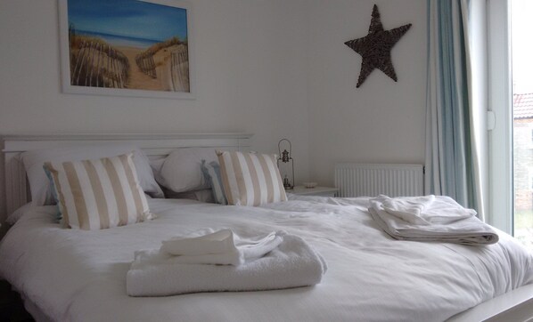 A neatly made bed with white bedding and striped pillows, a star decoration on the wall, and a painting of a beach scene above the bed.