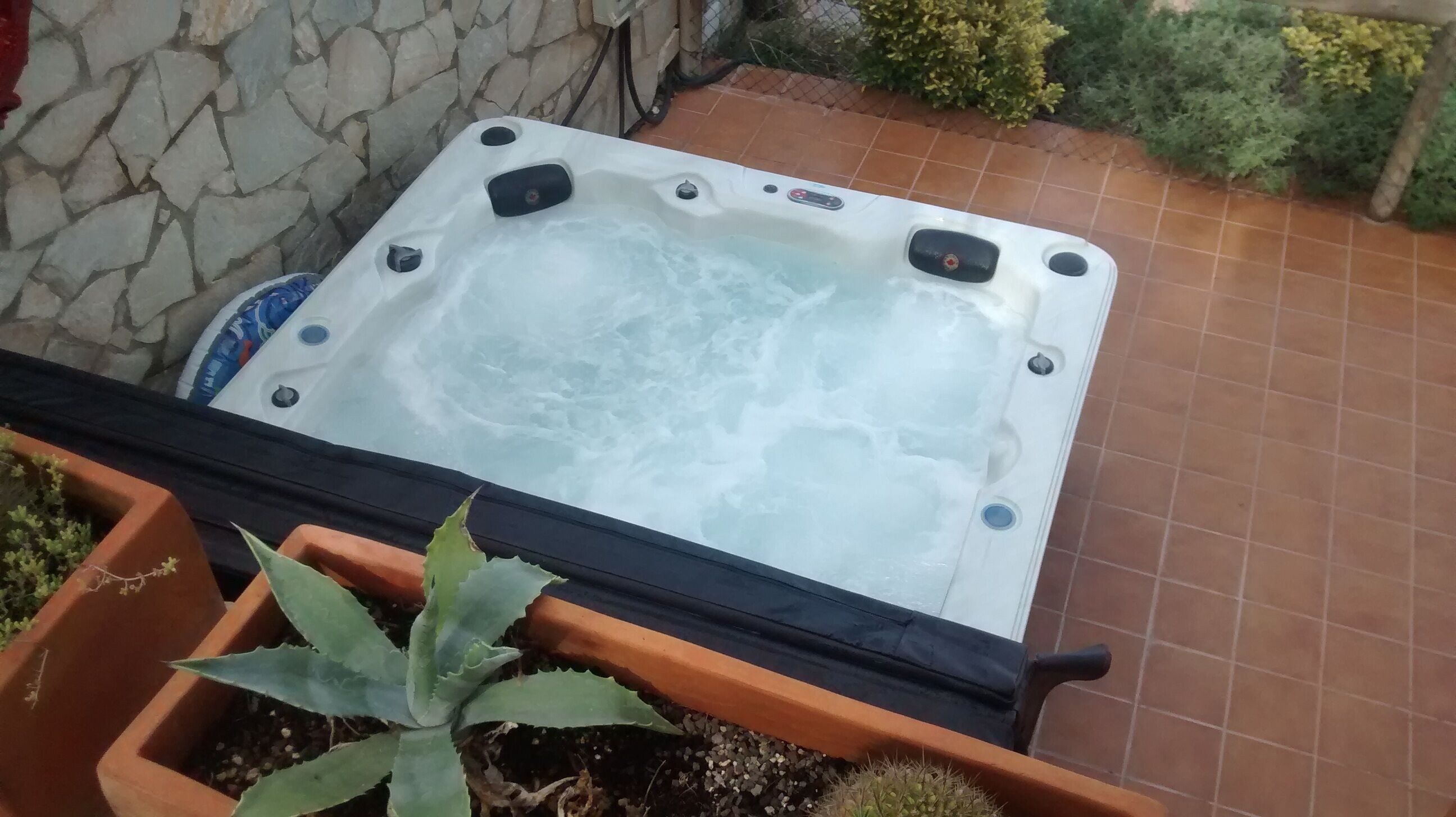 A hot tub with a black cover, surrounded by a stone wall and potted plants.