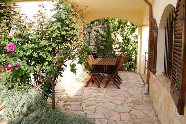 An outdoor patio with stone flooring, a wooden table and chairs, and a pergola with climbing plants. - Spacious Villa with Pool, Jacuzzi, Stunningly Situated on the Med (Begur)