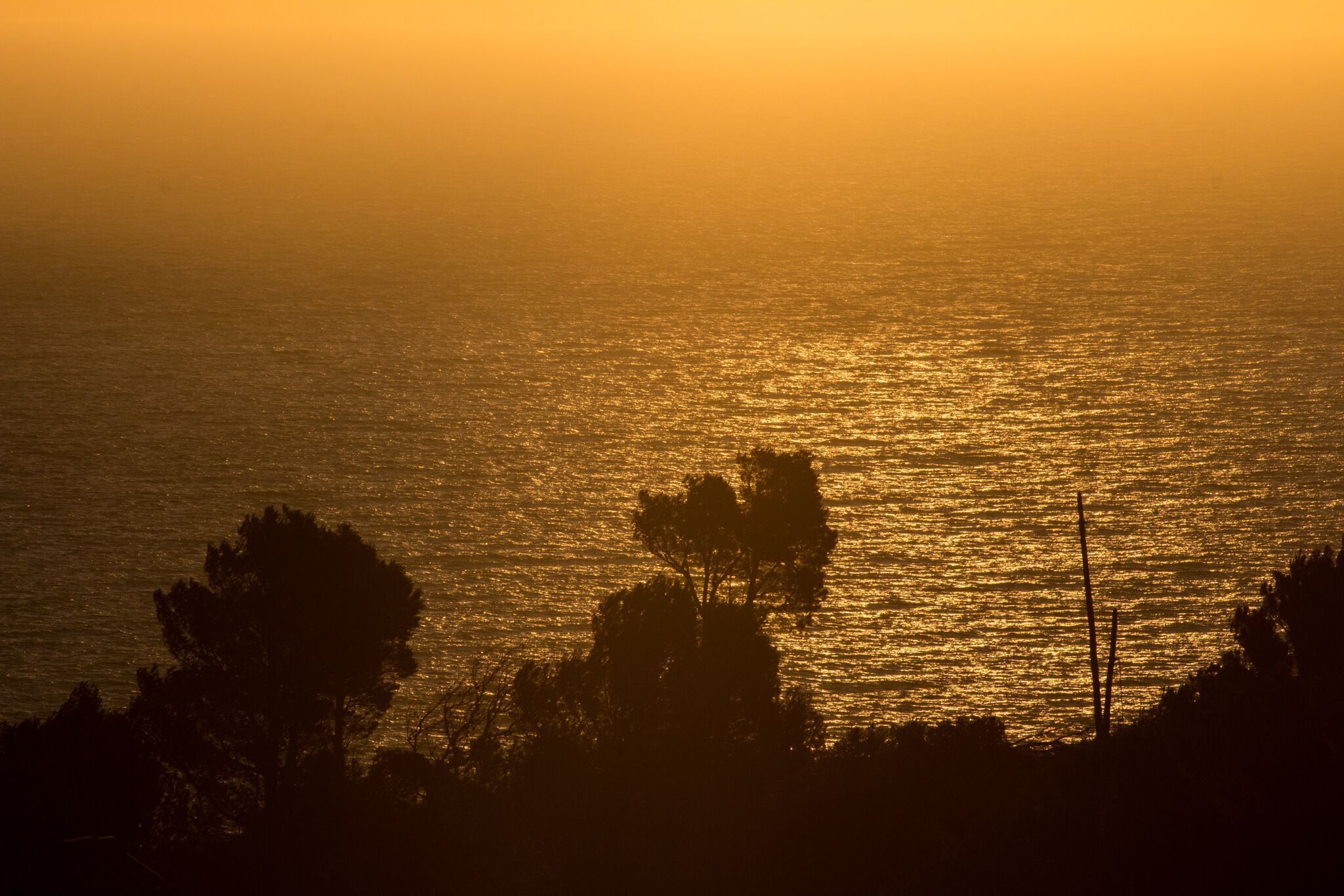 A sunset over a body of water with silhouettes of trees and a power line.