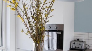 Eine Küche mit weißen Schränken, einem Edelstahlbackofen, einem Toaster und einer Vase mit Zweigen und gelben Blumen auf der Arbeitsfläche.