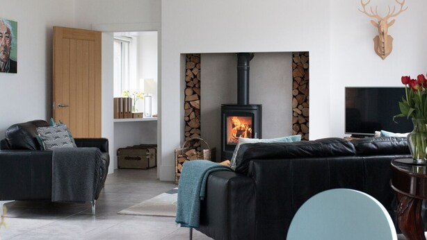 Ein modernes Wohnzimmer mit Kamin, schwarzen Ledersofas, einem Fernseher und einem Hirschgeweih an der Wand.