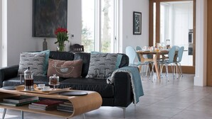 Ein modernes Wohnzimmer mit einem schwarzen Sofa, einem Couchtisch und einem Essbereich mit Holztisch und Stühlen.