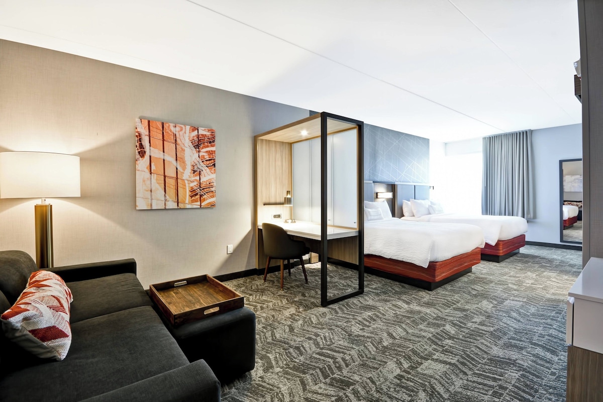 A hotel room with a sofa, a desk, a bed, and a large mirror.