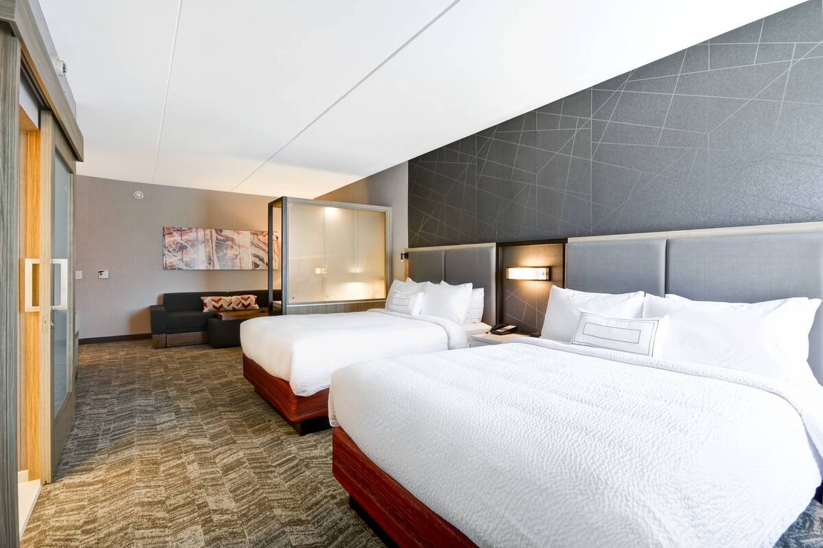 Ein Hotelzimmer mit zwei Betten, einem Schlafsofa, einem Schreibtisch und einem großen Fenster.