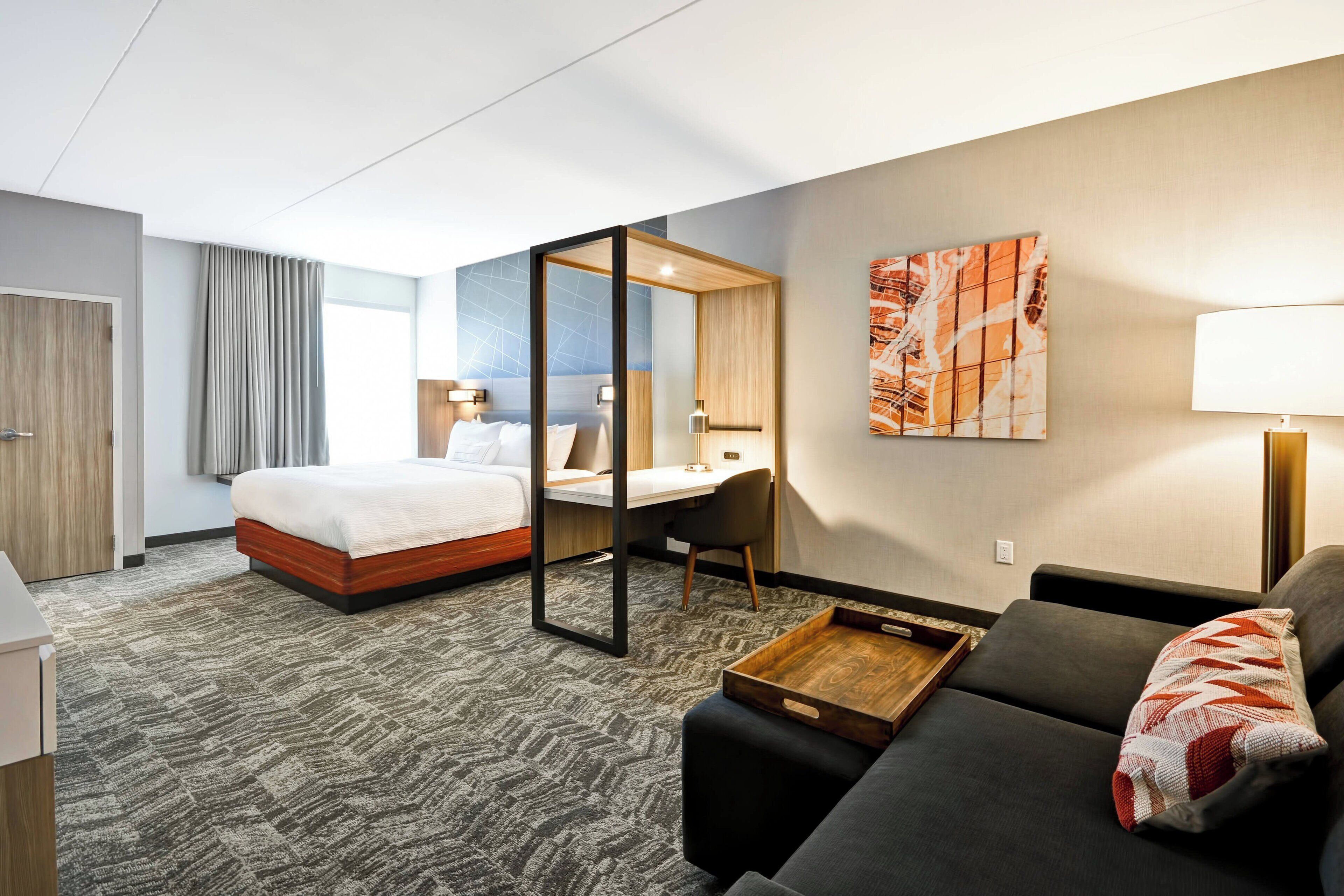 A hotel room with a bed, a desk, a sofa, and a large window.