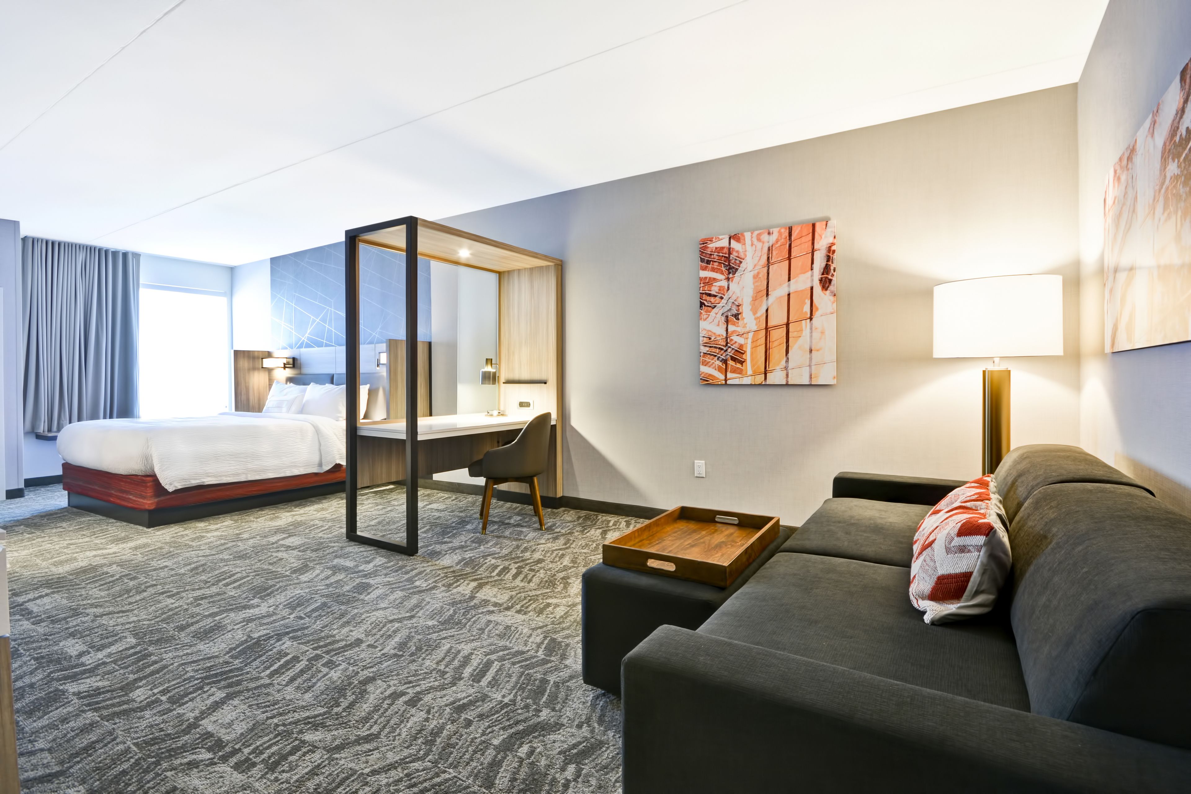 Una habitación de hotel con cama, escritorio, sofá, silla y un ventanal grande.