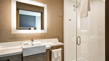 A modern bathroom with a large mirror, two sinks, a glass shower enclosure, and a towel rack.