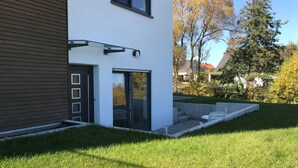A modern two-story house with a glass door and a small outdoor seating area. - New apartment in a quiet location in the recreation area (Schömberg)