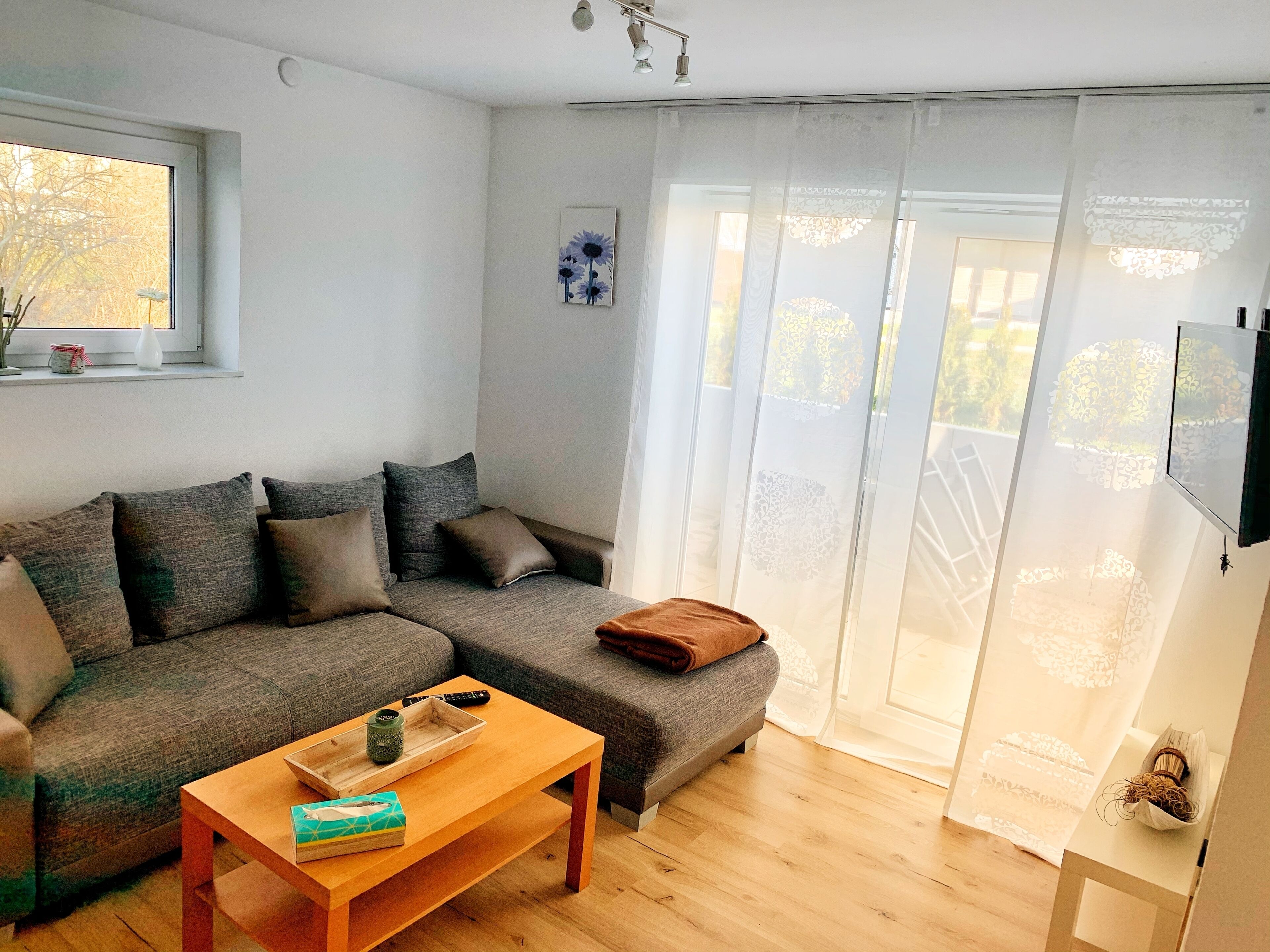 Una sala de estar moderna con un sofá seccional gris, una mesa de centro de madera y un ventanal corredero que da a un balcón.