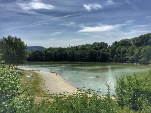Blick auf ein Seeufer mit Sandstrand, Bäumen und einem Boot auf dem Wasser.