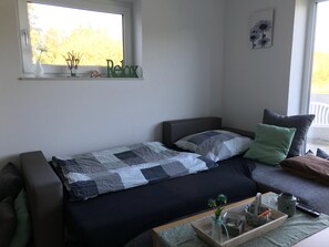 A small, cozy room with a bed, a window, a small table, and a couch.
