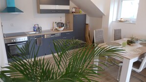 A modern kitchen with grey cabinets, a built-in oven, and a sink. There is a dining table with a white tablecloth and a vase of flowers. - New apartment in a quiet location in the recreation area (Schömberg)