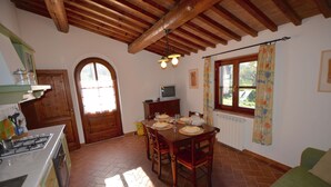 Une cuisine avec une table à manger pour quatre personnes, des placards en bois, une cuisinière et une fenêtre avec des rideaux.