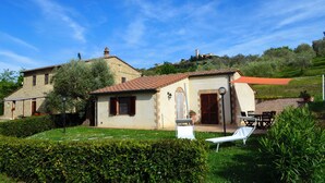 Une maison en pierre avec un toit en tuiles, une petite dépendance attenante et une pelouse avec un transat.