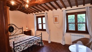 Une chambre à coucher avec un lit, une table et une chaise. Il y a des fenêtres avec des rideaux et un plafond en bois.