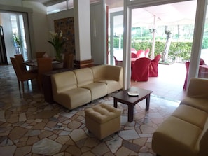 A lobby with a beige sofa, a coffee table, and a dining area with chairs and a table.