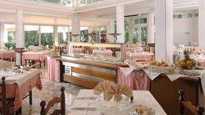 Ein großzügiger Essbereich mit mehreren Tischen und Stühlen, ein zentral gelegener Buffet mit verschiedenen Speisen und große Fenster, die für natürliches Licht sorgen.