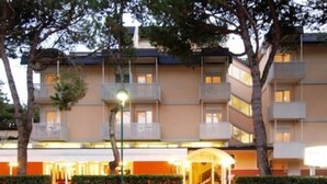 Ein mehrstöckiges Hotel mit Balkonen, einem überdachten Eingang und einem gepflegten Garten.