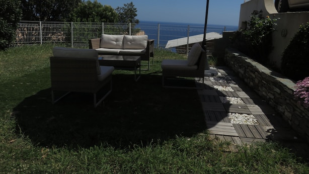 Eine Terrasse im Freien mit Tisch und Stühlen, einem großen Sonnenschirm und Blick aufs Meer.