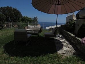 Eine Terrasse im Freien mit Tisch und Stühlen, einem großen Sonnenschirm und Blick aufs Meer.