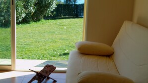 Ein Zimmer mit einem weißen Sofa, einem Holzstuhl und Blick auf einen Rasen durch eine Glastür.