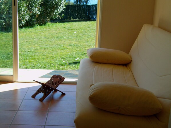 Ein Zimmer mit einem weißen Sofa, einem Holzstuhl und Blick auf einen Rasen durch eine Glastür.