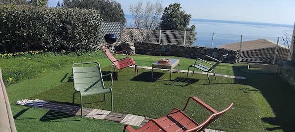 A backyard with artificial grass, a barbecue grill, and outdoor furniture.