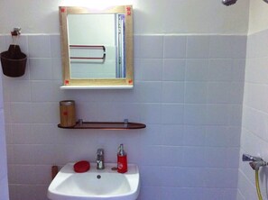Un baño con un lavabo blanco, un espejo y un dispensador de jabón rojo.