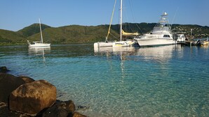 Un port de plaisance avec des bateaux amarrés, une eau claire et un paysage vallonné en arrière-plan.