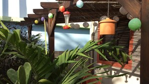 Une pergola en bois, ornée de lanternes en papier suspendues et agrémentée d’une fontaine en métal.