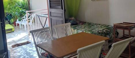 Una habitación con una mesa de comedor, sillas, un ventilador de techo, una cama con dosel verde y un cuadro de plantas tropicales.