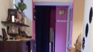 Passadís estret amb terra de fusta que condueix a una habitació amb parets morades i una porta.