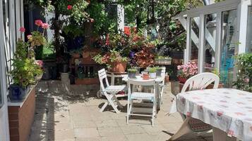 Un espace patio aménagé avec une table et des chaises, entouré de plantes en pot et d’une variété de fleurs.