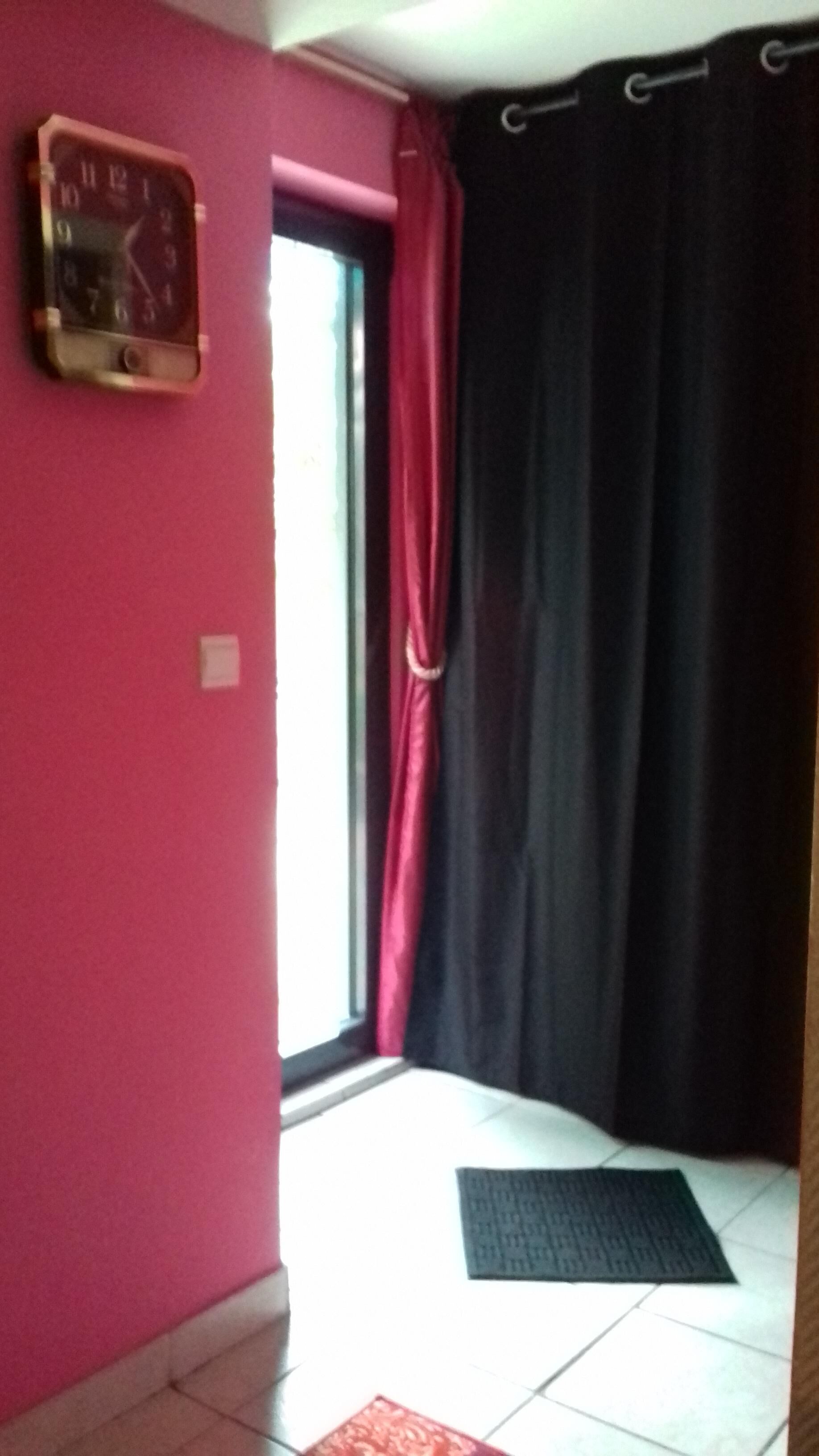 Quarto com parede rosa, um relógio, uma janela com cortinas pretas e um tapete preto no chão.
