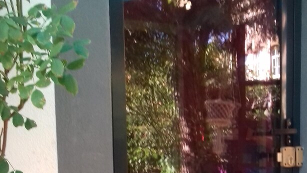 Una porta de vidre dona pas a una zona de pati amb una tenda blava, plantes en testos i mobles d'exterior.