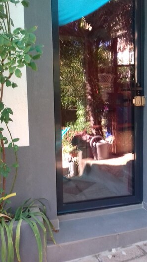 A glass door leading to a patio area with a blue awning, potted plants, and outdoor furniture.