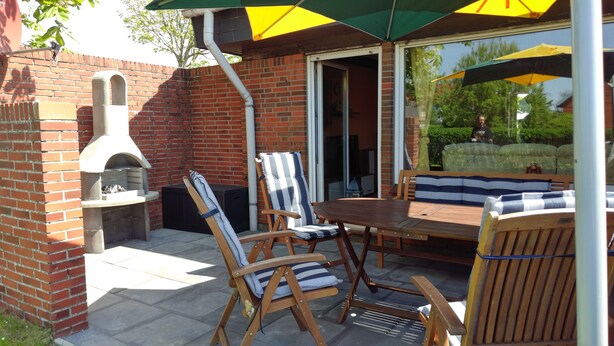 Eine Terrasse im Freien mit einer Ziegelwand, einem Holztisch, gestreiften Stühlen und einem Grill.