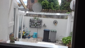 A small courtyard with a white wall, a blackboard with decorative items, a blue scooter, and a trash bin. - Comme chez vous prés sur la route des vins! (Mutzig)