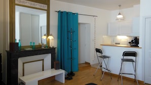 A compact living space with a kitchenette, a bench, a chair, a mirror, and a curtain.