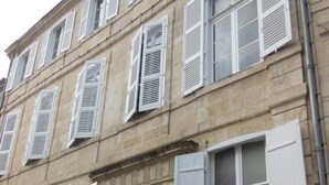 A historic building with a central entrance, multiple windows with shutters, and a stone facade.