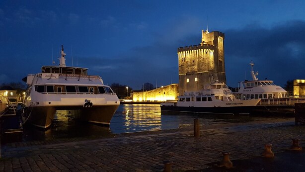 A historic stone tower and two boats docked at a waterfront.